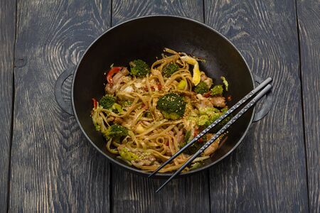 Traditional Asian dish - noodles with meat and vegetables in wok, on wooden surfaceの写真素材