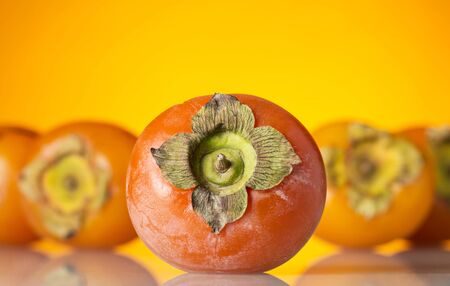 Tarnished persimmon fruit close - up, on bright yellow backgroundの写真素材