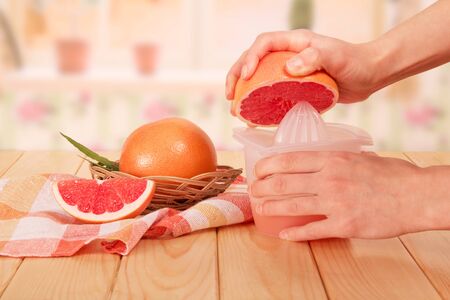 Basket with grapefruit and a piece of the next, women's hands holding a half grapefruit and a juicer with the juice, a towel on the kitchen background.の写真素材