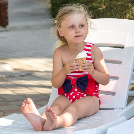 Cute little girl in swimsuit eating ice cream, sitting in deckchairの写真素材