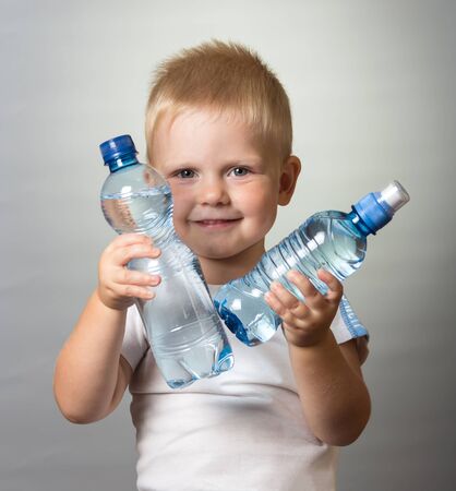 A smiling boy holds in his hands two bottles of water, on gray backgroundの写真素材