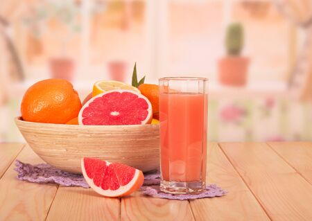 A bowl of whole and parts of citrus, a glass of grapefruit juice and a slice closeup on the background of the kitchen.の写真素材
