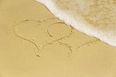 Sandy coast. Inscription two hearts on the beach in sea foamの写真素材