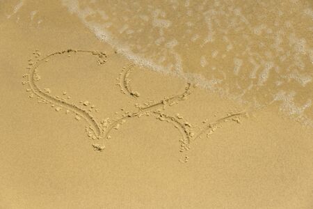 Sea foam washes the symbol of two hearts on the sandの写真素材