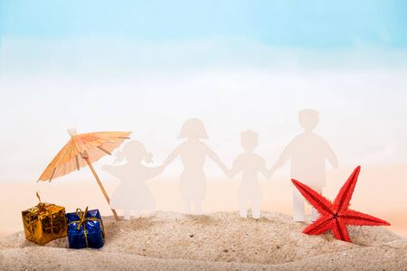 Paper figures joined hands - a symbol of a friendly family, an umbrella, gifts and a starfish in the sand against the background of the sea.の写真素材