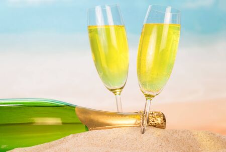 Bottle and two glasses with champagne in the sand against the background of the sea.の写真素材