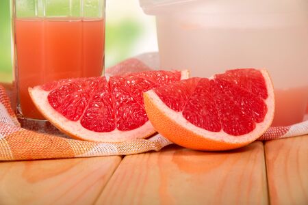 Pieces of grapefruit, a glass of juice and a napkin on a wooden tableの写真素材