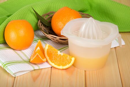 Hand press with squeezed juice, orange in basket, on wooden tableの写真素材