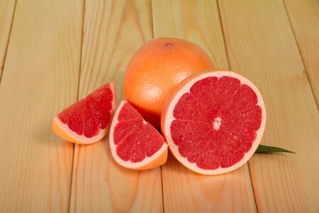 Whole grapefruit and chopped pieces on wooden tableの写真素材