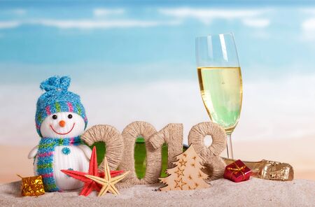 New Year inscription 2018, a bottle and a glass of champagne, snowman, gifts, starfish in the sand on the beach.の写真素材