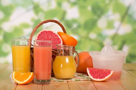 Jug and glasses full of juice, basket with citrus on background of  tableの写真素材
