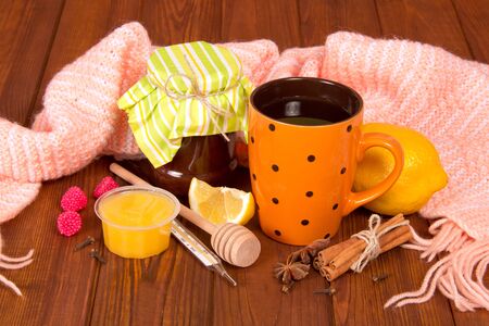 Cup of hot tea with lemon and honey from cold, a warm scarf on background of wooden tableの写真素材