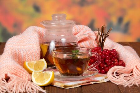 Bunch of viburnum, cup of hot tea with lemon from cold, on wooden tableの写真素材