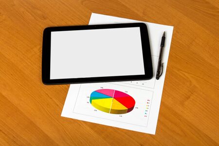 Tablet, a pen and a sheet of paper with a graph on the desktop background.の写真素材