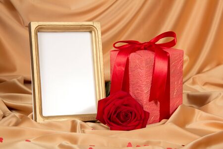 Box with gift, scarlet rose and frame for photo on background of beige silk fabricの写真素材