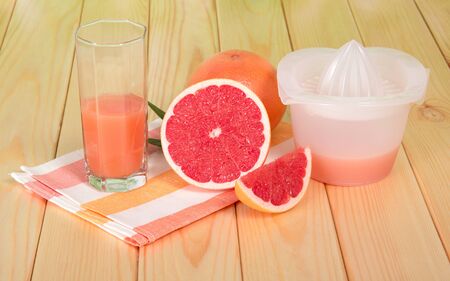 Juicer, grapefruit juice in glass, whole fruit and slices on wooden tableの写真素材