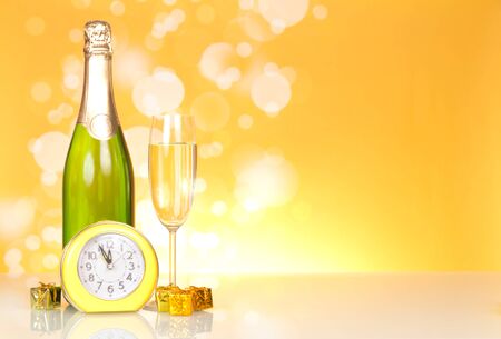 Bottle with champagne, small New Year surprises and clock on yellow backgroundの写真素材