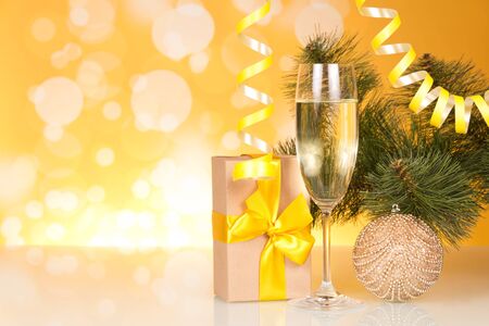 Champagne in wine glass, New Year's gift and decorated pine   branch, on yellow backgroundの写真素材
