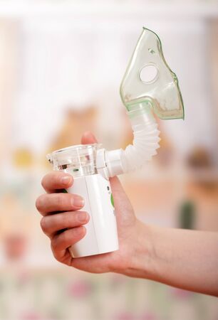Ultrasonic nebulizer with adapter and mask in female hand, on light backgroundの写真素材