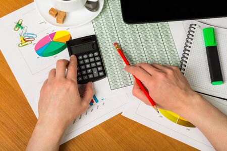 Female hands holding calculator and pencil, notebook, marker, accounts and charts, a tablet, a Cup of coffee on the desktop background.の写真素材