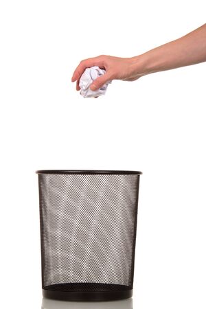 Empty shopping basket for paper waste and a female hand holds a ball of crumpled paper isolated on white background.の写真素材