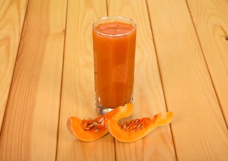 Pumpkin pieces and a glass of pumpkin juice on a light wood background.の写真素材