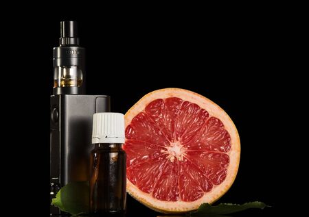 Electronic cigarette and aromatic liquid for smoking, slice of grapefruit isolated on black backgroundの写真素材
