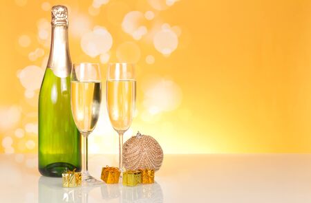 Bottle of champagne and New Year's gifts, on yellow sparkling backgroundの写真素材