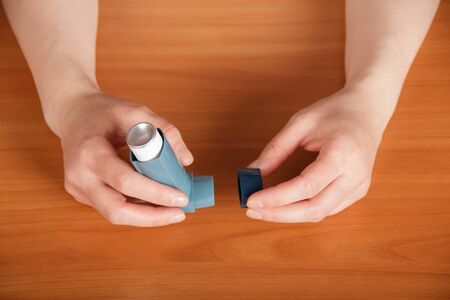 Female hands holding inhaler aerosol on the background of the table.の写真素材