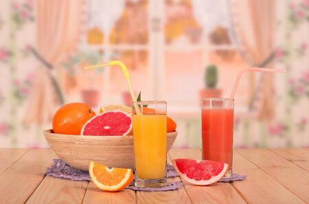 A bowl of citrus fruit, glasses of orange and grapefruit juices and straws, pieces of fruit on the kitchen background.の写真素材