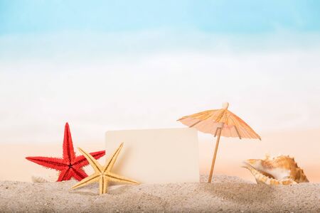 Blank card, starfish, umbrella and sea shell close-up in the sand against the background of the sea.の写真素材