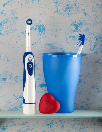 Electric, and usual toothbrush in glass, small heart, on blue backgroundの写真素材