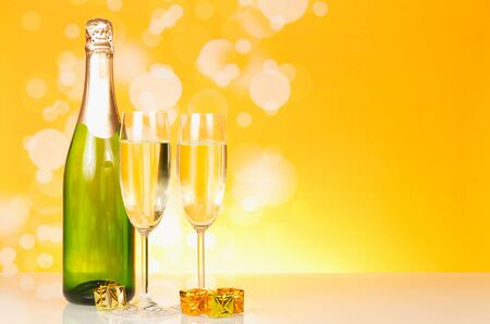 Bottle of champagne, wine glasses, small boxes with souvenirs on bright yellow backgroundの写真素材