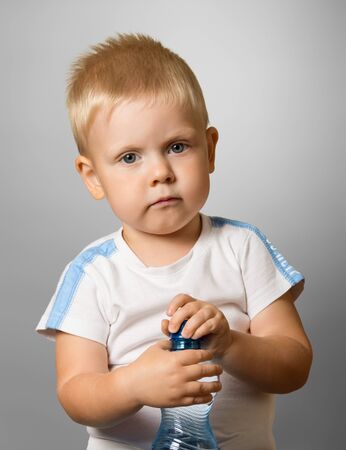 Charming baby holding a bottle with water, on gray backgroundの写真素材