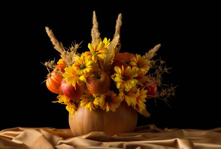 Original composition of apples and flowers in pumpkin on silk fabric, isolated on black backgroundの写真素材