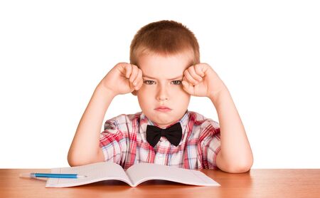 Sad little boy sits at the table next to the notebook and pen isolated on white backgroundの写真素材