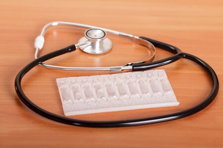 Medical diagnostic tool stethoscope and packing of ampoules, on background of wooden tableの写真素材