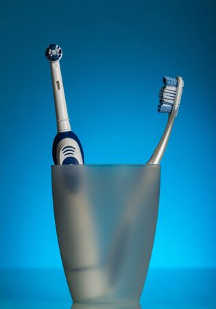 Two toothbrushes in the glass, electric and manual, on blue backgroundの写真素材