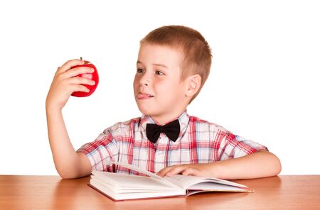 Boy reading book at table, in hand red Apple, isolated on whiteの写真素材