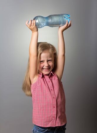 Little girl laughing and holding bottle over his head, on gray backgroundの写真素材