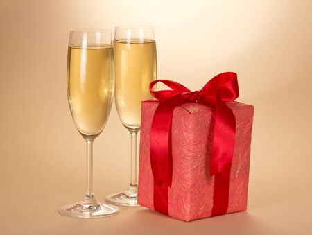 Christmas gift in red box with bow and two glasses of champagne, on beige backgroundの写真素材
