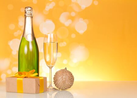 Bottle of champagne, glass of wine, Christmas toys and gift, on bright yellow backgroundの写真素材