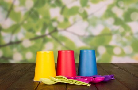 Three colored disposable Cup, nearby to many spoons, on wooden brown tableの写真素材