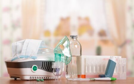 Compressor nebulizer and small pocket inhaler, medication, pills, thermometer on background of tableの写真素材