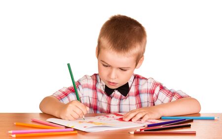 Boy in shirt with bow tie is drawing sitting at table, isolated on white backgroundの写真素材