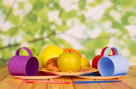 Set of disposable plastic utensils, an apple and croissant in plate, on wooden tableの写真素材