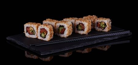 Sushi-rolls with seafood in sesame seeds on plate isolated on black backgroundの写真素材