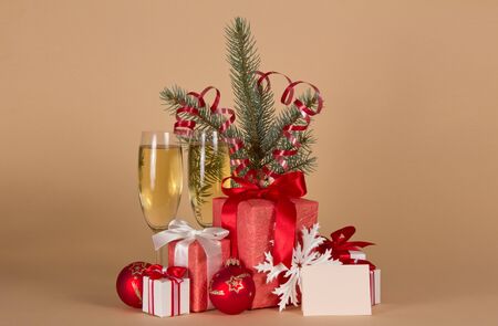 Glass with champagne, boxes with gifts, Christmas toys and blank card for congratulations, on beige backgroundの写真素材