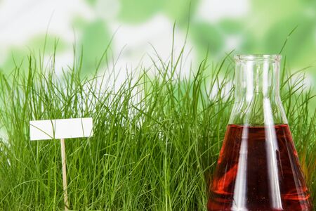 Flask with liquid fertilizer on background of green grass and blank card for writingの写真素材