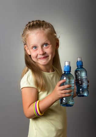 Two bottles of clean water in hands of small, smiling girl on grey backgroundの写真素材